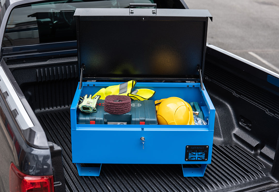 Blue metal tool box open with a range of electrical tools inside and a yellow hard hat. The toolbox is on the back of a pick up van.