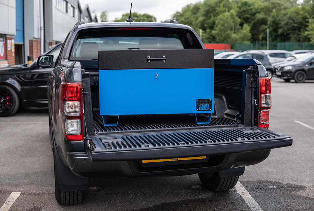 Large blue metal tool box closed with a black lid on the back of a 4x4 pick up truck.