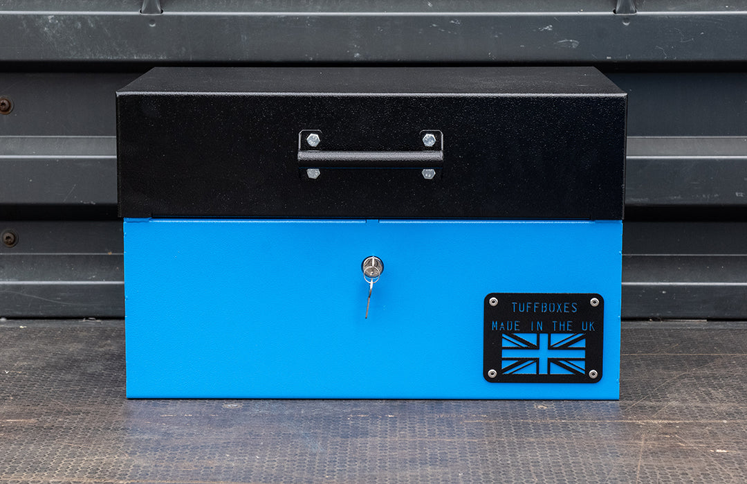 Small blue metal tool box closed with a black lid on the back of a flat bed truck.