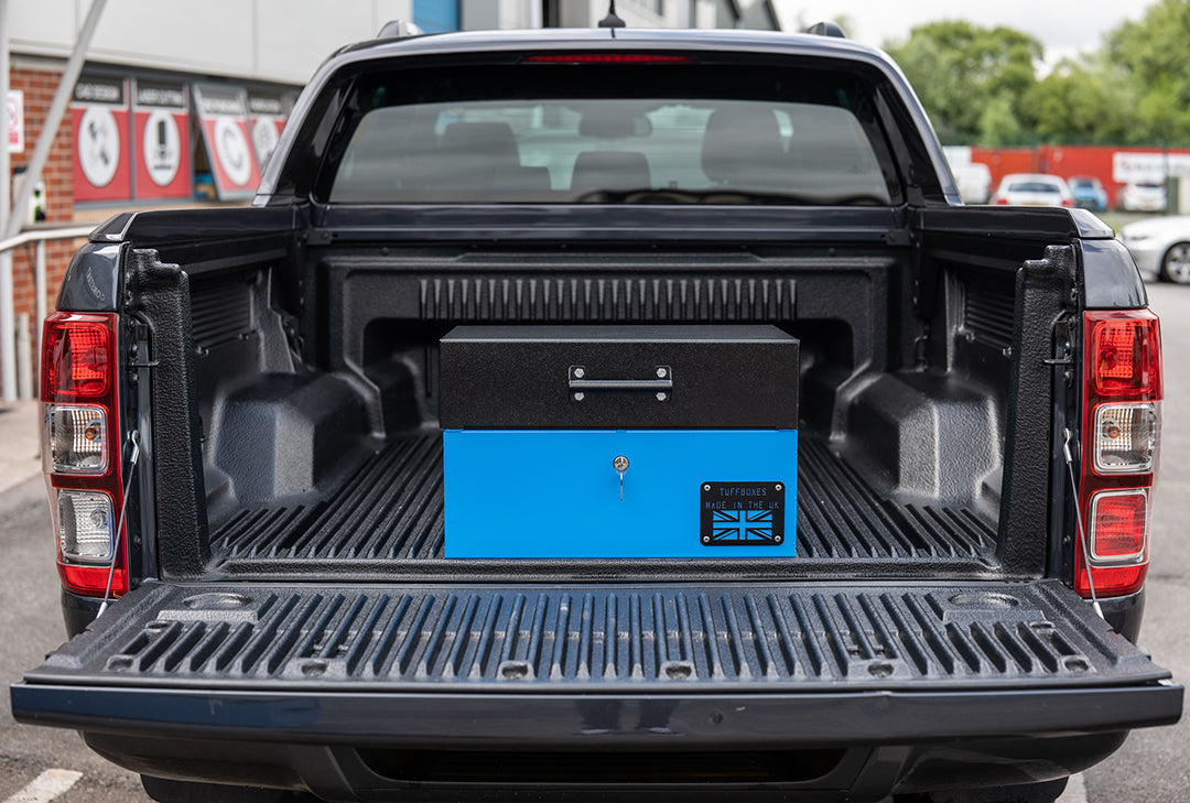 Small Blue metal tool box closed with a black lid on the back of a 4x4 pick up truck.