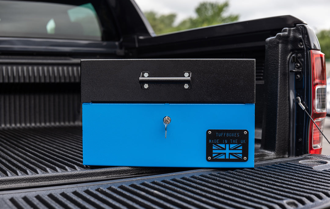 Small Blue metal tool box closed with a black lid on the back of a 4x4 pick up truck.