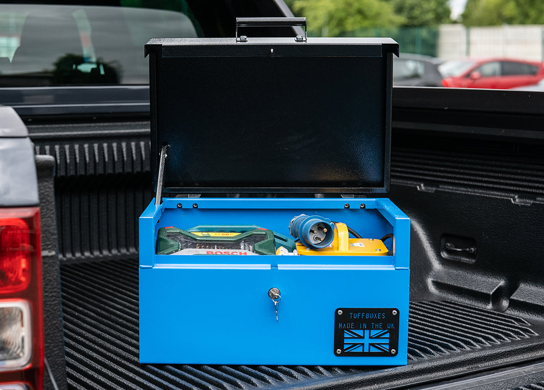 Small blue metal tool box  with a range of electrical tools inside and a yellow hard hat. The toolbox is on the back of a pick up van.