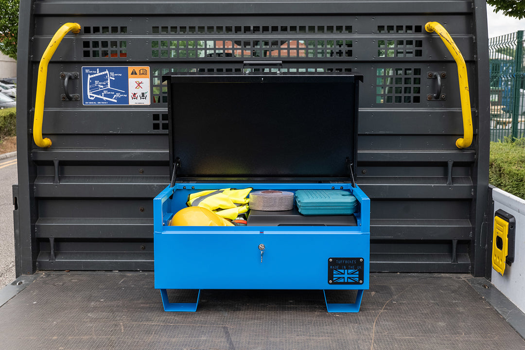 Blue metal tool box open with a range of electrical tools inside and a yellow hard hat. The toolbox is on top of a flat bed truck.